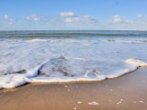 the beach and ocean water coming up the sand and blue sky with clouds in the background